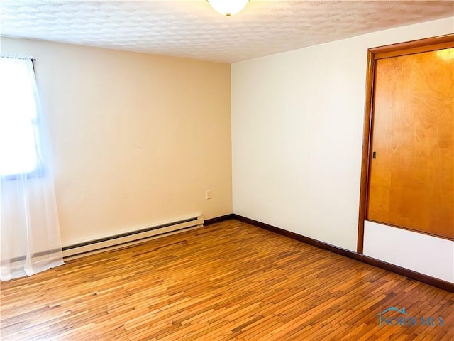 empty room featuring a textured ceiling, a baseboard heating unit, baseboards, and wood-type flooring