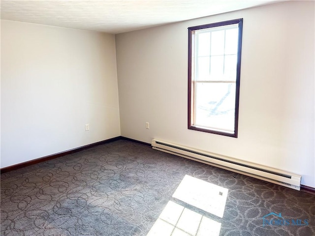 spare room featuring a baseboard heating unit, baseboards, and dark carpet