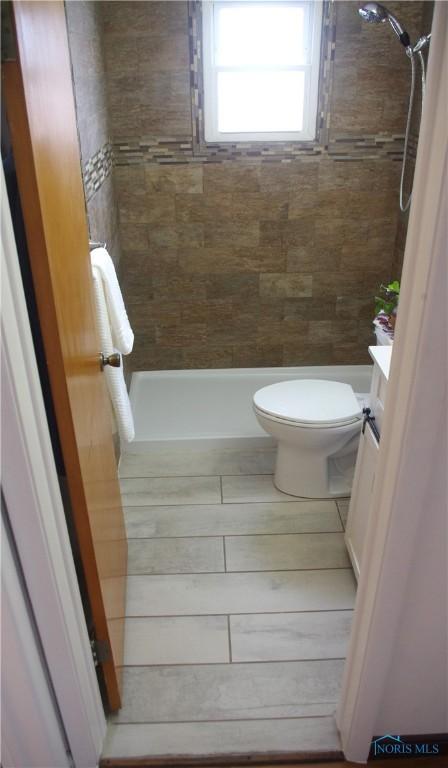 full bath featuring tiled shower and toilet