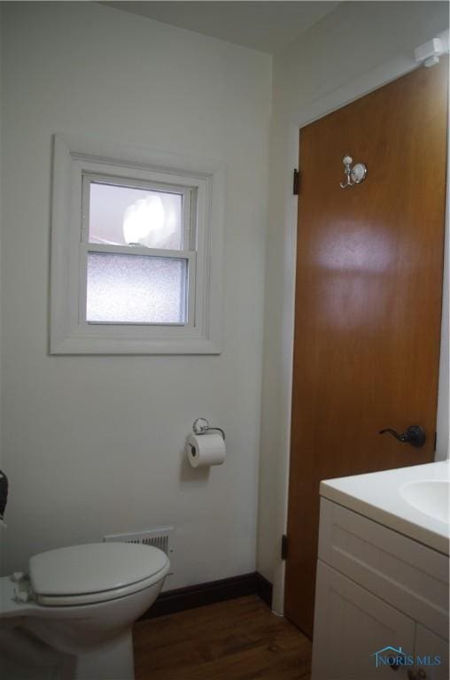 half bath featuring vanity, wood finished floors, visible vents, baseboards, and toilet