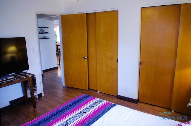 bedroom featuring wood finished floors, baseboards, and two closets