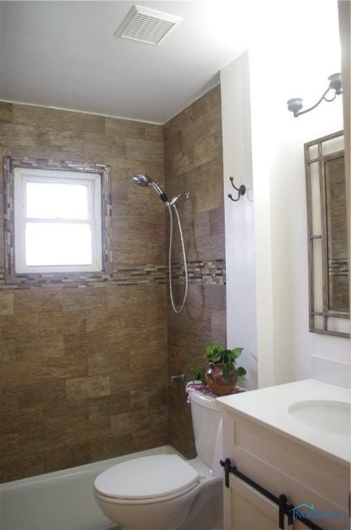 bathroom with vanity, toilet, visible vents, and tiled shower