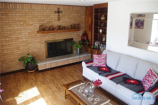 living area with a fireplace, wood finished floors, and brick wall