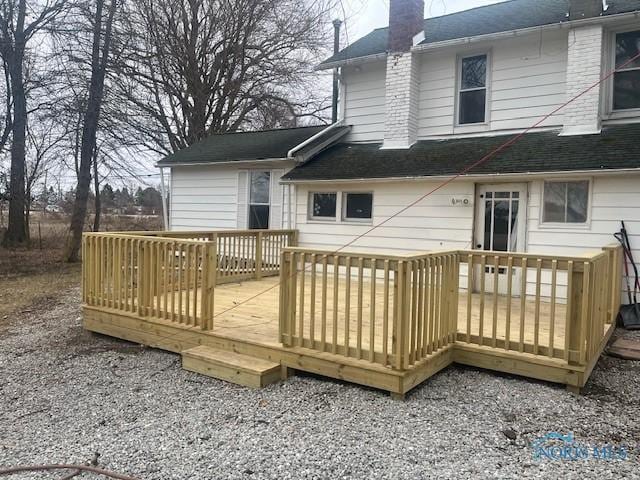 back of house with a deck, a shingled roof, and a chimney