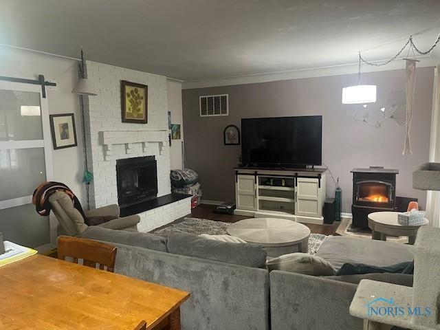 living room featuring visible vents, ornamental molding, a barn door, a fireplace, and a wood stove