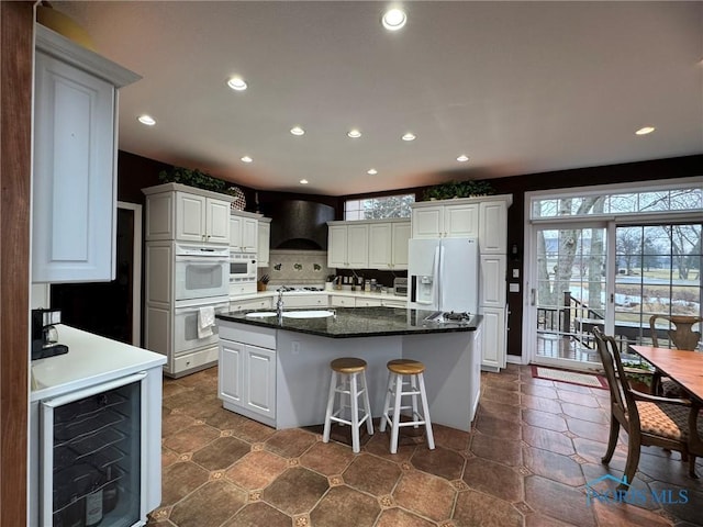 kitchen featuring custom exhaust hood, plenty of natural light, white appliances, and beverage cooler