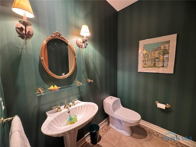 half bath featuring tile patterned floors, toilet, wallpapered walls, and baseboards