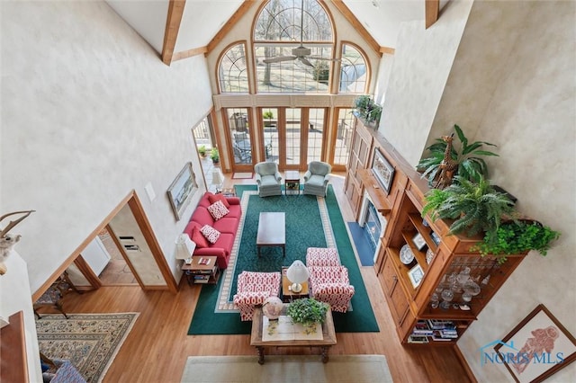 living area with beam ceiling, high vaulted ceiling, wood finished floors, and a fireplace