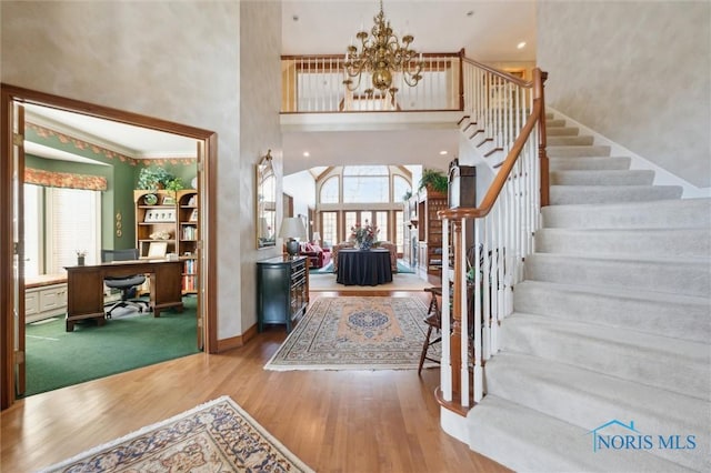 foyer with baseboards, stairway, a high ceiling, wood finished floors, and a notable chandelier