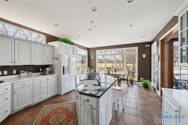 kitchen featuring a center island, plenty of natural light, white refrigerator with ice dispenser, and a sink
