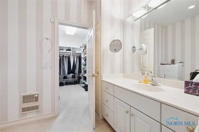 bathroom with heating unit, vanity, wallpapered walls, baseboards, and a spacious closet