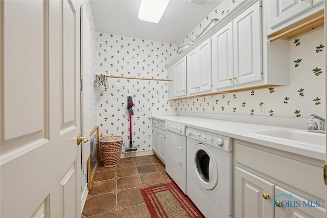 clothes washing area with dark tile patterned floors, a sink, cabinet space, wallpapered walls, and washing machine and clothes dryer