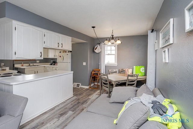 kitchen with a notable chandelier, white cabinetry, white appliances, light wood finished floors, and light countertops