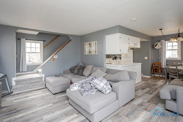 living area featuring baseboards, arched walkways, stairs, light wood-type flooring, and a chandelier