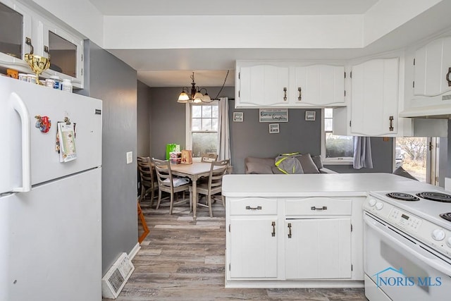 kitchen with an inviting chandelier, white appliances, white cabinetry, and a peninsula