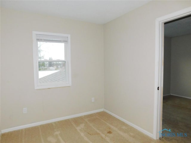 spare room with baseboards and light colored carpet