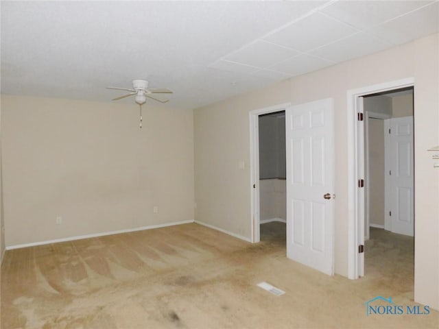 unfurnished bedroom with a walk in closet, carpet flooring, a ceiling fan, and baseboards