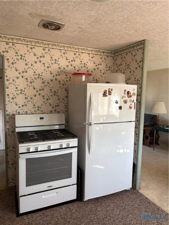 kitchen with white appliances, a textured ceiling, and wallpapered walls