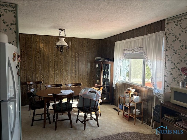 dining room featuring wooden walls, light colored carpet, and a textured ceiling