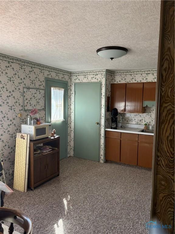 kitchen featuring wallpapered walls, light countertops, brown cabinets, and a textured ceiling