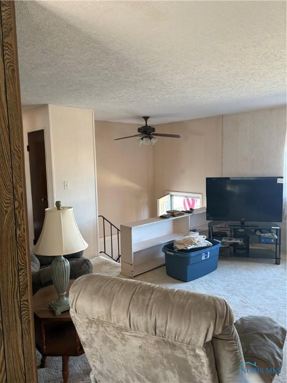 carpeted living area with a textured ceiling and ceiling fan