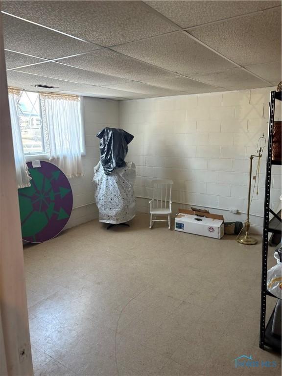 interior space with tile patterned floors, a drop ceiling, and concrete block wall