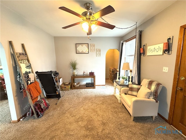 living area featuring arched walkways, ceiling fan, baseboards, and carpet