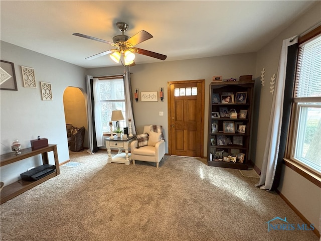 sitting room with visible vents, light carpet, arched walkways, baseboards, and ceiling fan