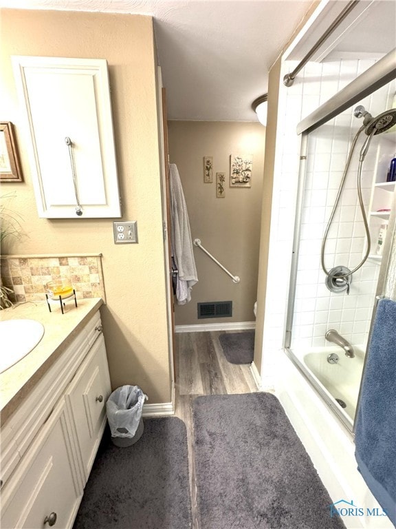 full bath featuring visible vents, baseboards, wood finished floors, shower / bath combination with glass door, and vanity