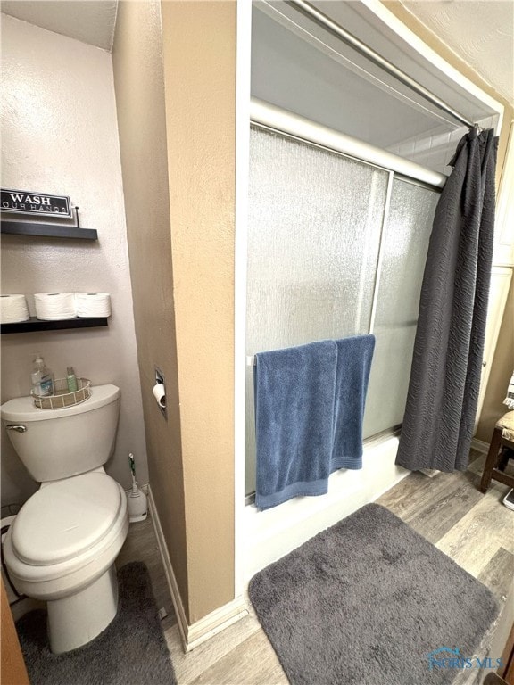 full bath featuring baseboards, toilet, wood finished floors, a stall shower, and a textured wall