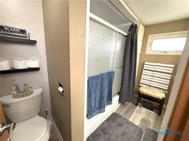 bathroom featuring toilet, wood finished floors, a stall shower, and baseboards