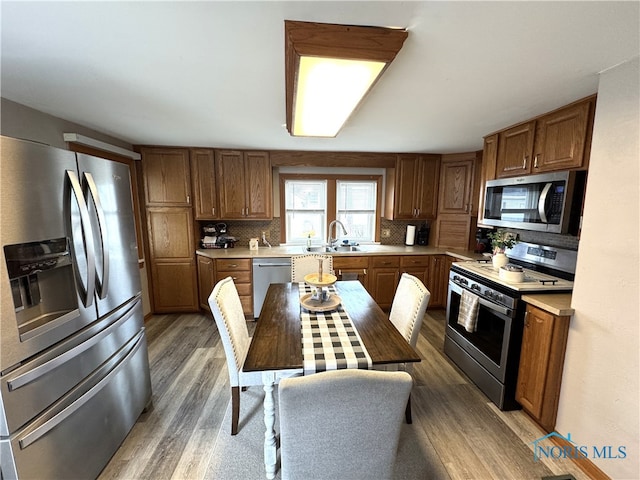 kitchen with tasteful backsplash, light countertops, appliances with stainless steel finishes, wood finished floors, and brown cabinetry