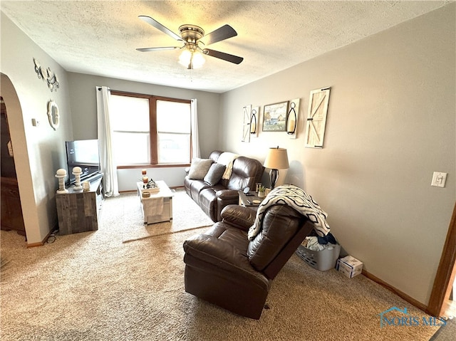 carpeted living room with arched walkways, a textured ceiling, baseboards, and a ceiling fan