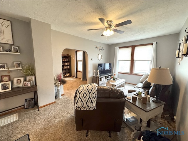 carpeted living room with a textured ceiling, baseboards, arched walkways, and ceiling fan