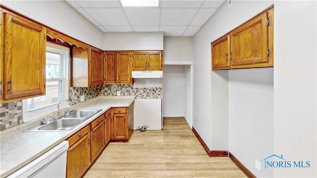 kitchen with under cabinet range hood, a sink, backsplash, brown cabinetry, and white dishwasher