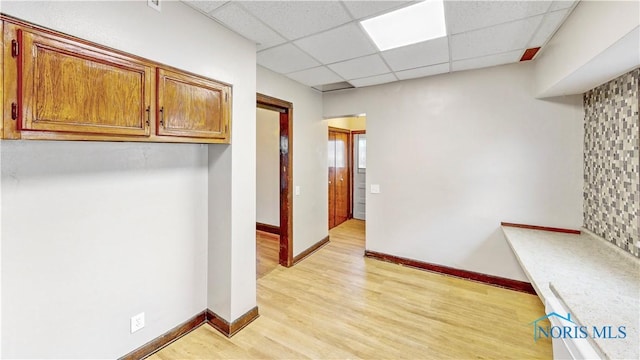 hallway featuring light wood finished floors, baseboards, and a drop ceiling