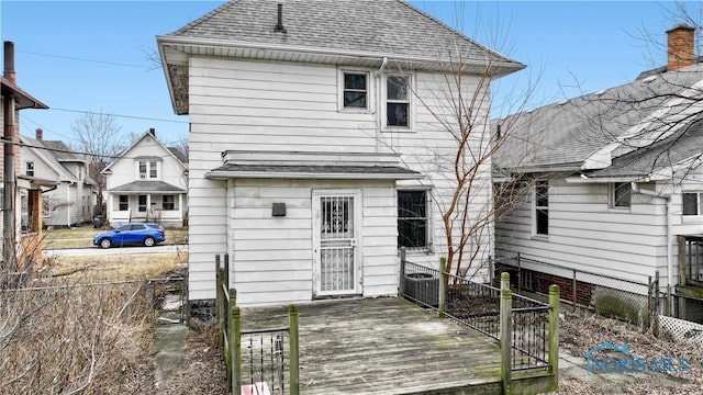 rear view of house with a deck, roof with shingles, and fence