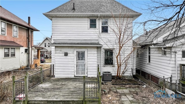 rear view of house featuring a wooden deck, cooling unit, a shingled roof, and fence