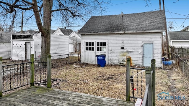 rear view of property with a deck, an outdoor structure, fence, and roof with shingles