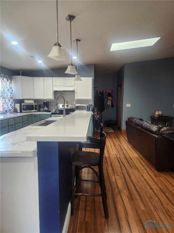 kitchen with stainless steel microwave, pendant lighting, light countertops, white cabinetry, and dark wood-style flooring