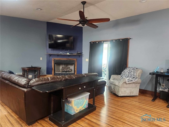 living room with lofted ceiling, a ceiling fan, wood finished floors, a fireplace, and baseboards