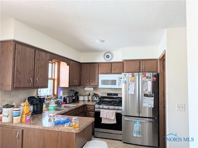 kitchen featuring a peninsula, a sink, stainless steel appliances, light countertops, and tasteful backsplash