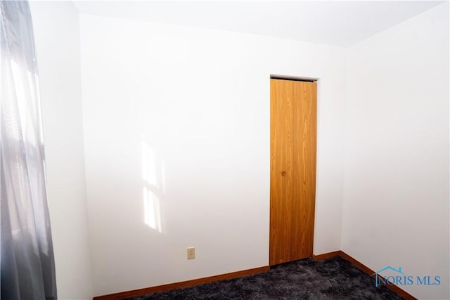 spare room featuring dark carpet and baseboards