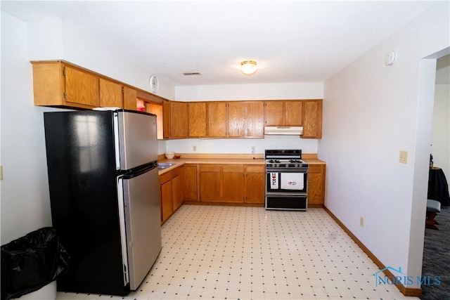 kitchen featuring brown cabinetry, range with gas cooktop, freestanding refrigerator, and light countertops