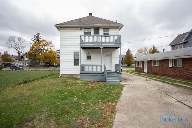 view of front of home with a balcony, a porch, a front yard, and fence