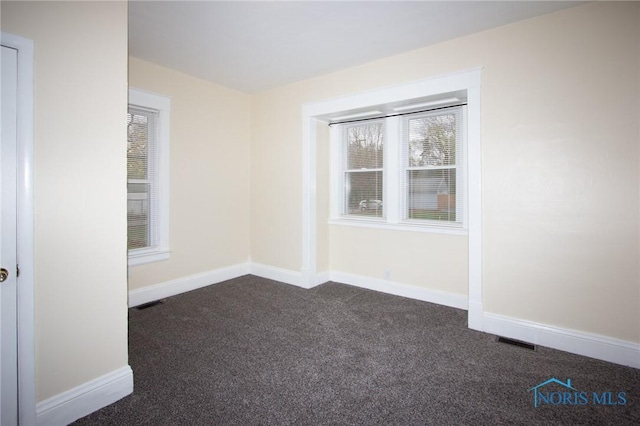 empty room featuring dark colored carpet, visible vents, and baseboards