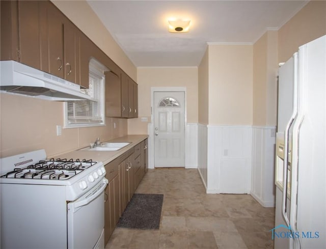 kitchen featuring white appliances, a wainscoted wall, a sink, light countertops, and under cabinet range hood