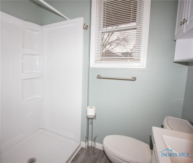 bathroom featuring toilet, wood finished floors, baseboards, and walk in shower