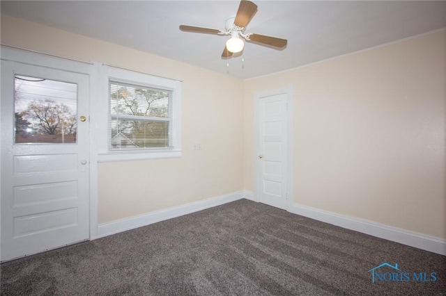 empty room with dark colored carpet, baseboards, and a ceiling fan