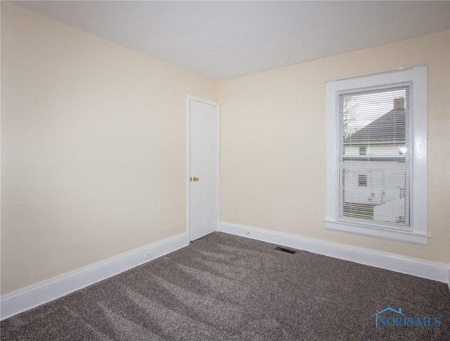 spare room with visible vents, baseboards, and dark carpet